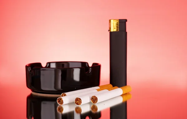 Cigarrillos, cenicero y encendedor sobre fondo rojo — Foto de Stock
