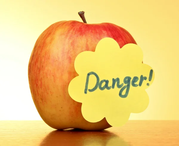 Een appel op gele achtergrond met "danger" sticker — Stockfoto