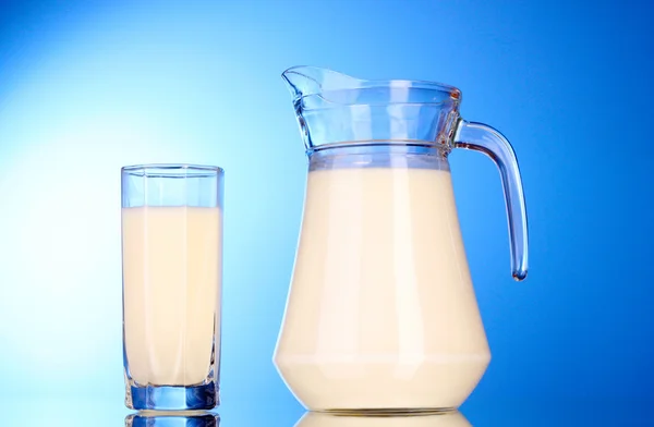 Jarro e vidro com leite no fundo azul — Fotografia de Stock