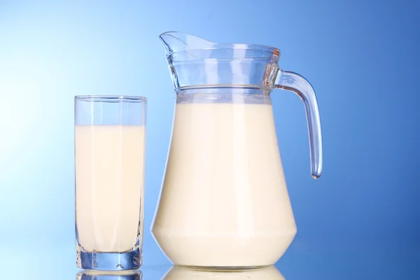 Jarra y vaso con leche sobre fondo azul — Foto de Stock
