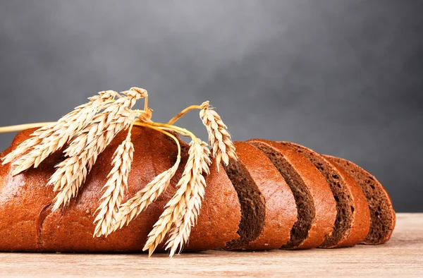 Rye bread and spikelets on wooden table on gray background — Stock Photo, Image