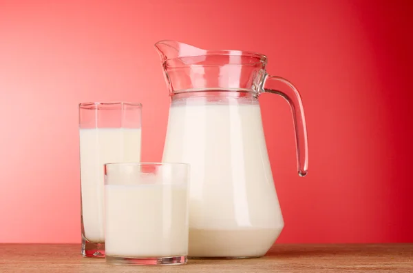 Tillbringare och glas med mjölk på röd bakgrund — Stockfoto