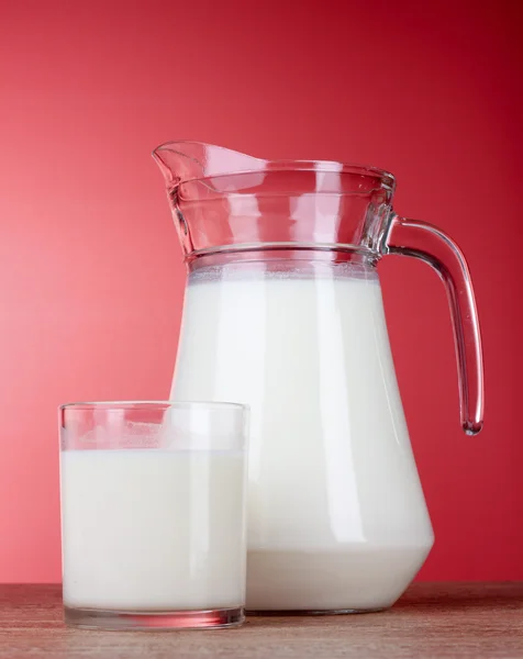 Tillbringare och glas med mjölk på röd bakgrund — Stockfoto