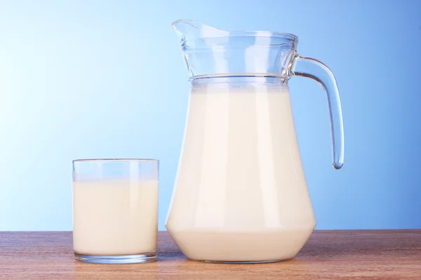 Džbán a sklenice s mlékem na modrém pozadí — Stock fotografie