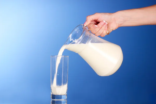 Iemand giet melk van een kruik in een glas op blauwe achtergrond — Stockfoto