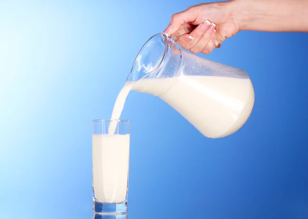 Jemand gießt Milch aus einem Krug in ein Glas auf blauem Hintergrund — Stockfoto