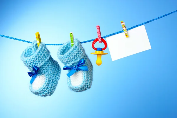 Botines de bebé, pezón y tarjeta blanca sobre un fondo azul —  Fotos de Stock