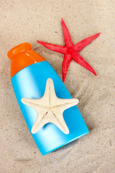 Bloqueador solar en botellas, conchas y estrellas de mar sobre arena —  Fotos de Stock