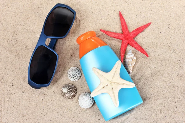 Bloqueador solar en botellas, conchas y estrellas de mar sobre arena — Foto de Stock