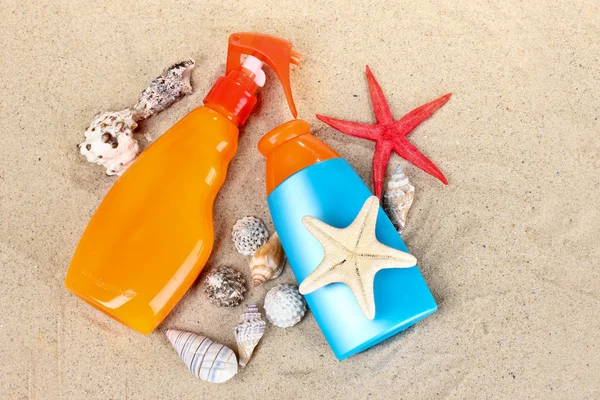 Protetor solar em garrafas, conchas e estrelas do mar na areia — Fotografia de Stock