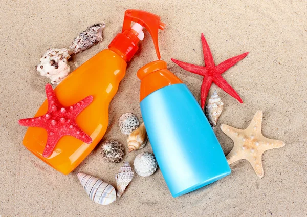 Bloqueador solar en botellas, conchas y estrellas de mar sobre arena —  Fotos de Stock