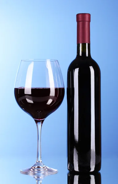 Botella de vino y copa sobre fondo azul — Foto de Stock