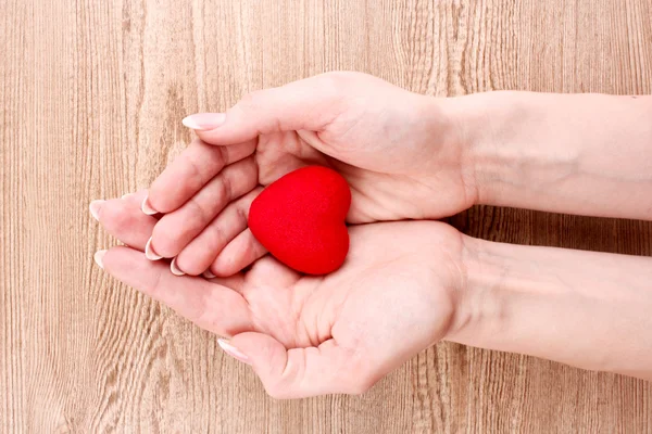 Coração vermelho nas mãos sobre fundo de madeira — Fotografia de Stock