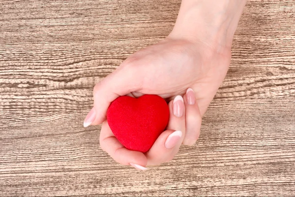 Coração vermelho nas mãos sobre fundo de madeira — Fotografia de Stock
