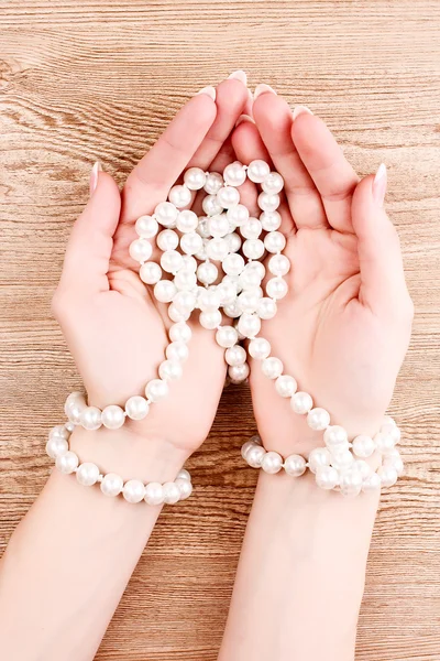 Frau Hand mit Perlen auf hölzernem Hintergrund — Stockfoto