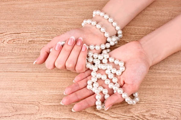 Frau Hand mit Perlen auf hölzernem Hintergrund — Stockfoto