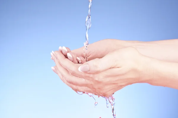Mänskliga händer med vatten stänk på dem med blå bakgrund — Stock fotografie