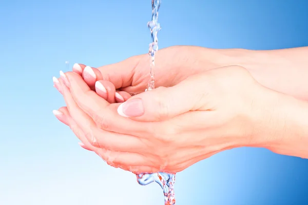 Mãos humanas com água espirrando sobre eles com fundo azul — Fotografia de Stock