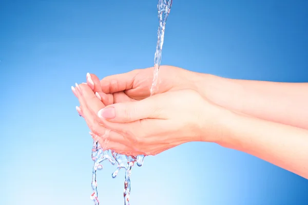 Mänskliga händer med vatten stänk på dem med blå bakgrund — Stock fotografie