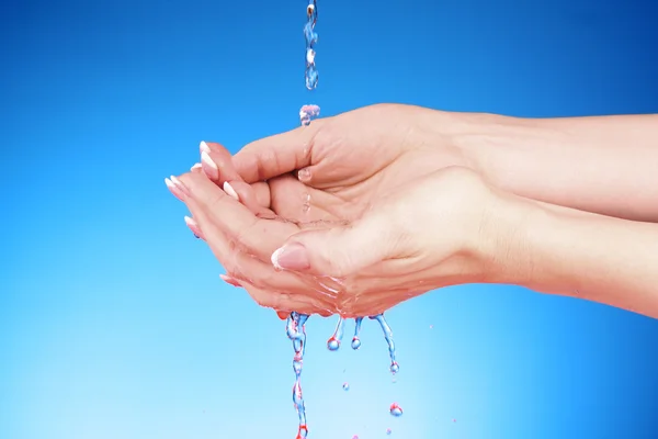Menschenhände mit Wasser, das auf sie mit blauem Hintergrund spritzt — Stockfoto