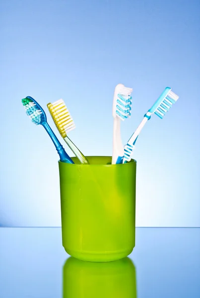 Четыре зубные щетки в пластиковой чашке на синем фоне — стоковое фото