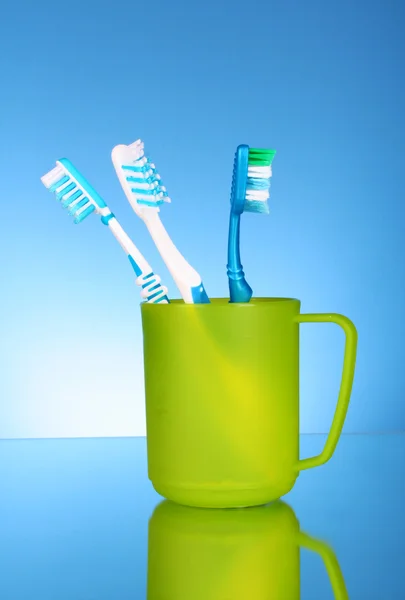 Four toothbrushes in plastic cup on blue background — Stock Photo, Image