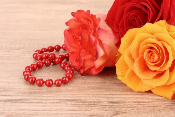 Three flowers and beads on wooden table — Stock Photo, Image