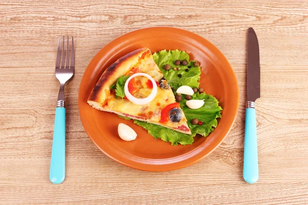 Пицца на тарелке и нож с вилкой на деревянном столе — стоковое фото