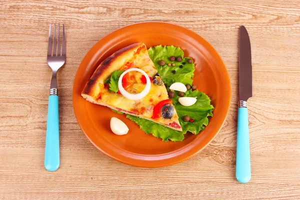 Pizza na placa e faca com garfo na mesa de madeira — Fotografia de Stock