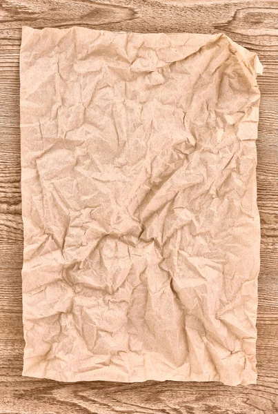 Brown crumpled paper on wooden texture — Stock Photo, Image