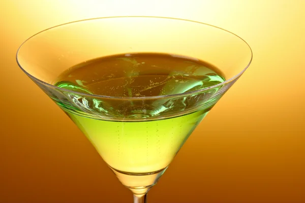 Glas mit grünem alkoholischen Getränk vor gelb-braunem Hintergrund — Stockfoto
