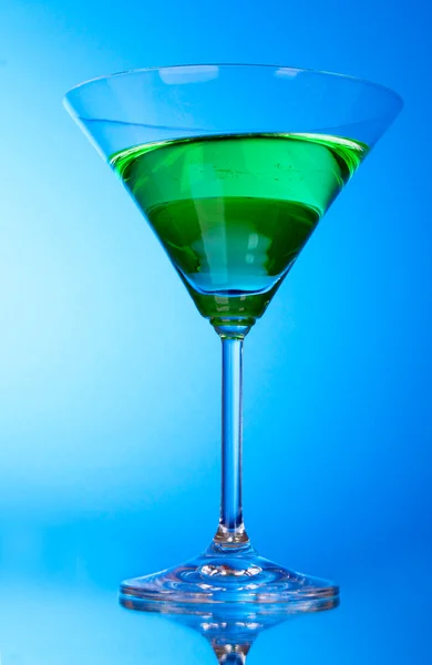 Склянка з зеленим алкогольним напоєм на синьому фоні — стокове фото