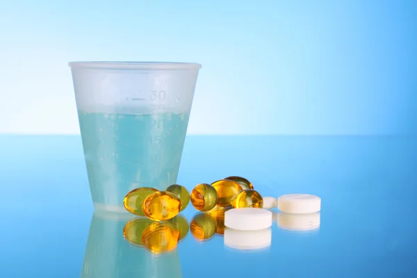 Wiele tabletek i szklankę wody na niebieskim tle — Zdjęcie stockowe