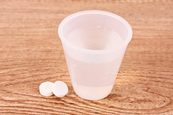 Två tabletter och glas vatten på träbord — Stockfoto