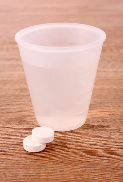 Дві таблетки і склянка води на дерев'яному столі — стокове фото