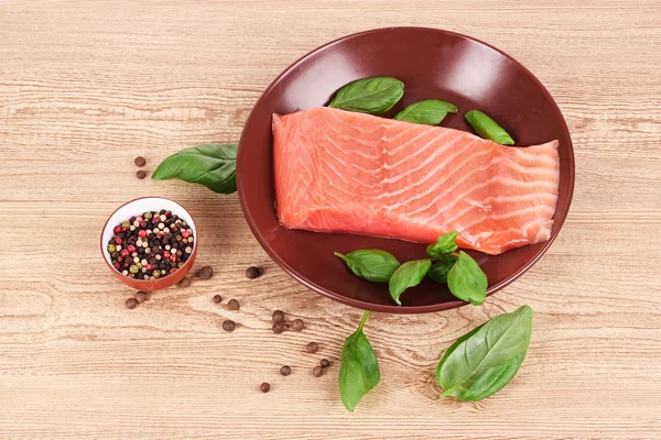 Červená ryba na talíři s pepřem a zelenými listy — Stock fotografie