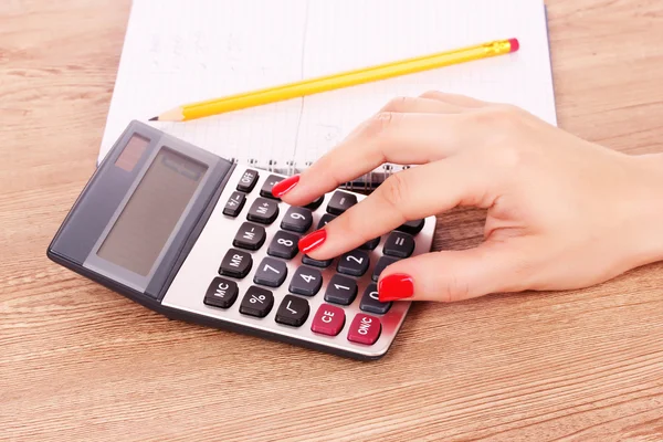 Mão, bloco de notas e calculadora em fundo de madeira — Fotografia de Stock