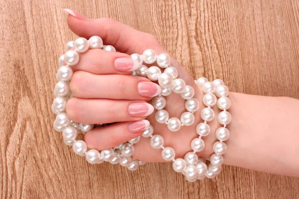Woman hand with pearls on wooden background Stock Picture