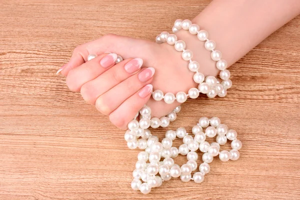 Woman hand with pearls on wooden background Royalty Free Stock Images