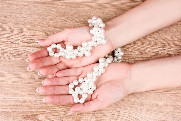 Woman hand with pearls on wooden background Stock Image
