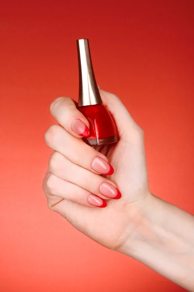 Verniz de unhas na mão em um fundo vermelho — Fotografia de Stock
