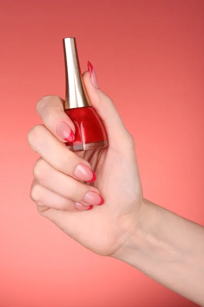 Лак для ногтей в руке на красном фоне — стоковое фото
