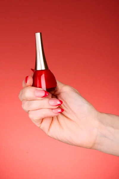 Nagellack in der Hand auf rotem Hintergrund — Stockfoto
