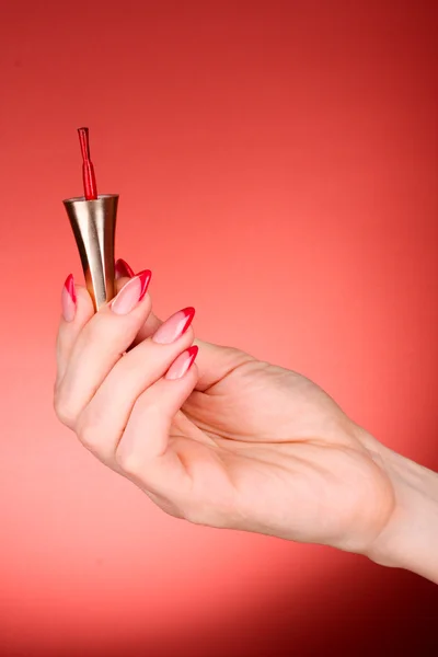 Nail polish brush in hand on a red background — Stock Photo, Image