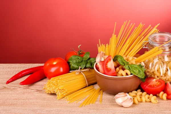 Spaghetti mit Knoblauch, Zwiebeln, Gewürzen und Basilikum auf rotem Hintergrund — Stockfoto