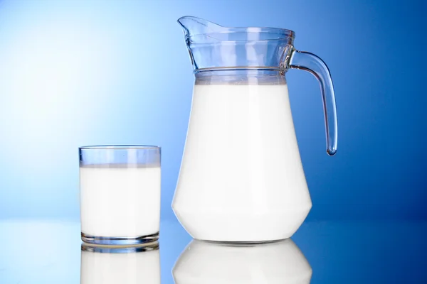 Brocca e bicchiere con latte su sfondo blu — Foto Stock