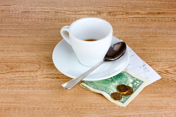 Empty cup of coffee with five dollars tip on wooden background.