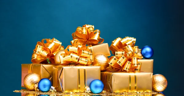 Hermosos regalos en envases de oro y bolas de Navidad en ba azul —  Fotos de Stock