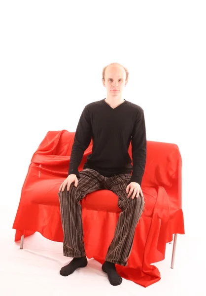 Beyaz izole kırmızı kanepede oturan genç adam — Stok fotoğraf