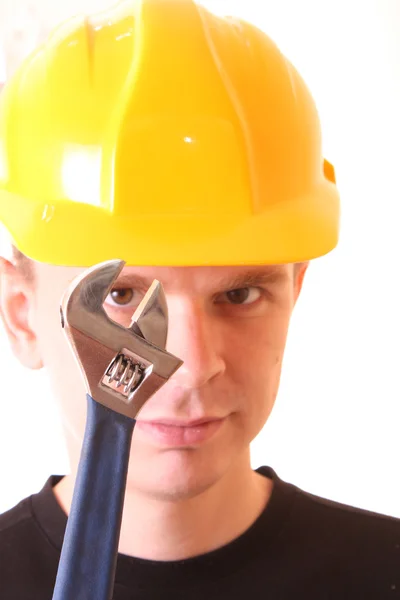 Young man with adjustable wrench in yellow helmet isolated on wh — Stock Photo, Image